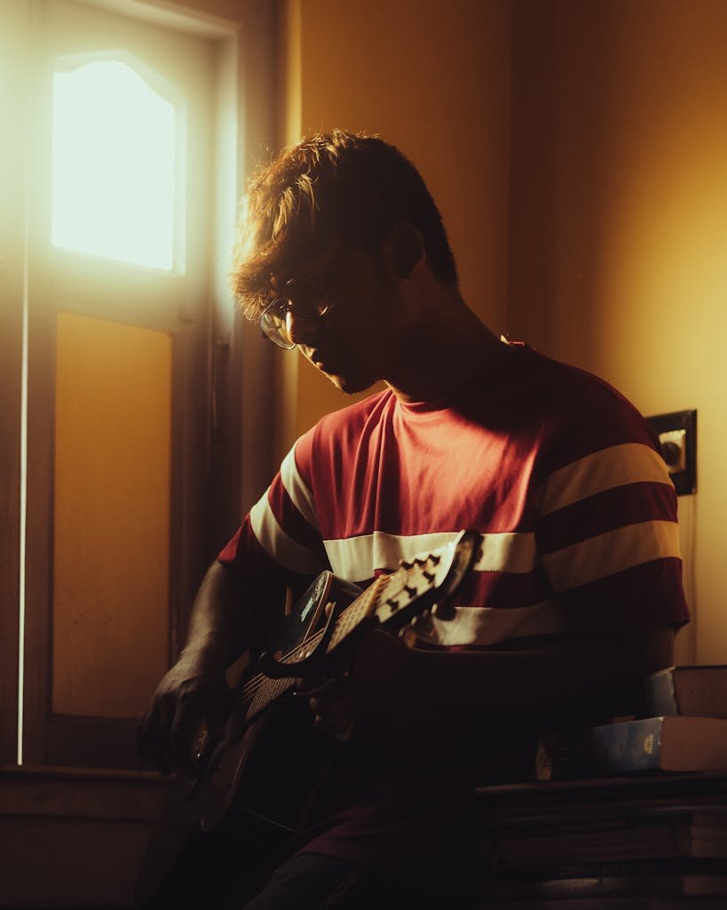 A person playing guitar by a window, bathed in warm sunlight, creating a peaceful ambience.